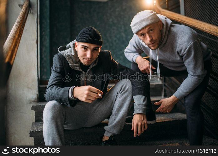 Two robbers waiting for victim on stairs and smoking. Street bandits, criminal. Robbery attack danger