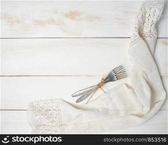 two rope-tied aluminum forks on a white wooden background, next to a cotton towel, top view,