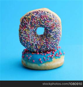 two round baked donut with colored sugar sprinkles and with blue sugar icing on a blue background