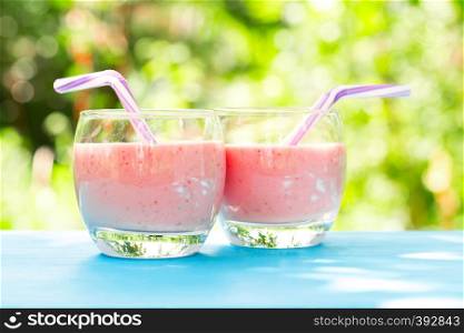 Two round glasses of berry smoothie or yogurt on the background of green foliage. Two round glasses of berry smoothie or yogurt on background of g