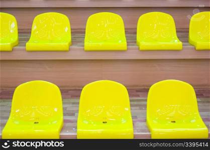 two rows of yellow plastic seats in a school gym, focus on the upper row