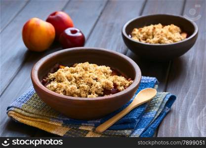 Two rustic bowls filled with baked plum and nectarine crumble or crisp, photographed on dark wood with natural light (Selective Focus, Focus one third into the first dessert)