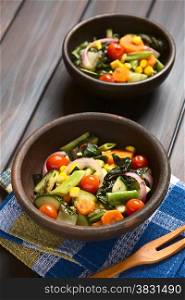 Two rustic bowls of baked vegetables (zucchini, onion, cherry tomato, broccoli, carrot, sweet corn, green bean, chard) seasoned with thyme, photographed on dark wood with natural light (Selective Focus, Focus one third into the first dish)