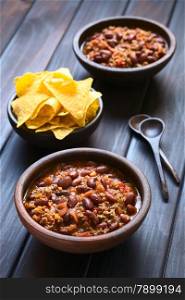 Two rustic bowls of chili con carne with tortilla chips in the back, photographed with natural light (Selective Focus, Focus in the middle of the chili)