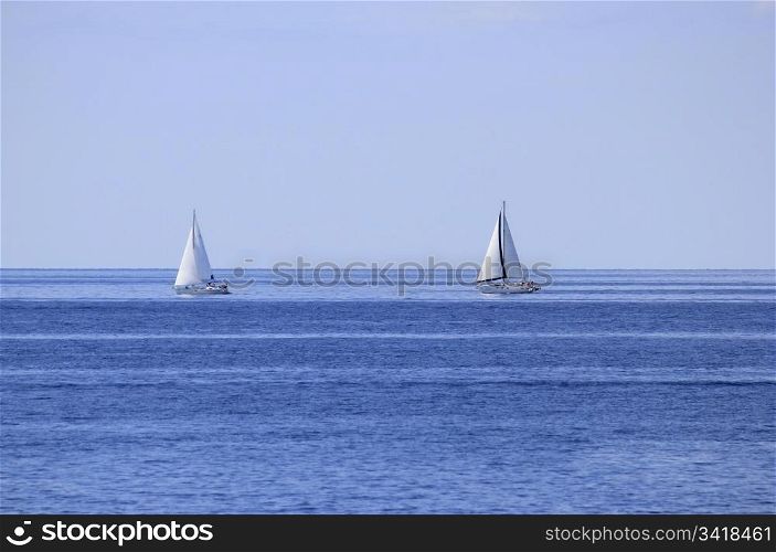 Two sailboats on open blue sea horizon