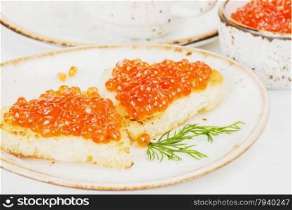 Two sandwiches heart shaped with red caviar on a porcelain plate