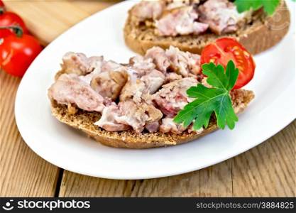 Two sandwiches of rye bread with brains, tomato and parsley on an oval plate on a wooden boards background