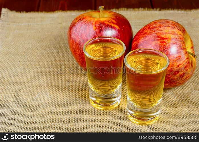 Two schnapps drinks and red apples on the rustic burlap background. Two schnapps drinks and red apples