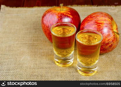 Two schnapps drinks and red apples on the rustic burlap background. Two schnapps drinks and red apples