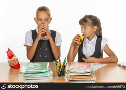 Two school friends drink juice at a table in a school class