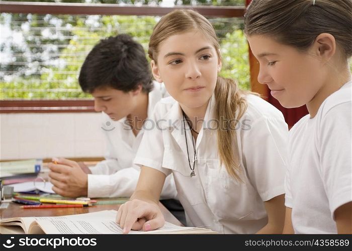Two schoolgirls and a schoolboy sitting in a classroom
