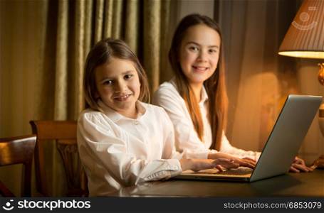 Two schoolgirls doing homework at laptop at night