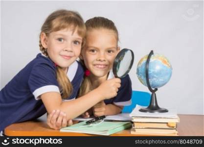 Two schoolgirls looking at globe through a magnifying glass