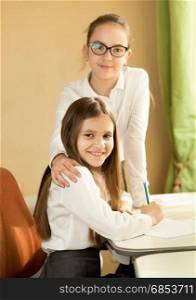 Two schoolgirls posing behind desk at bedroom
