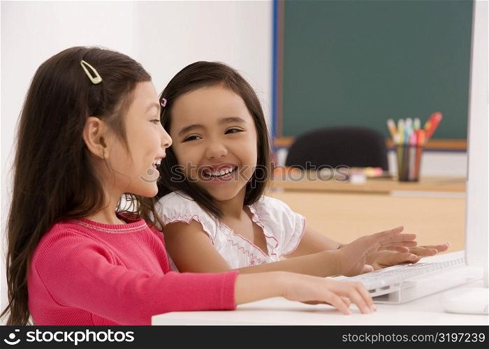 Two schoolgirls smiling in front of a computer