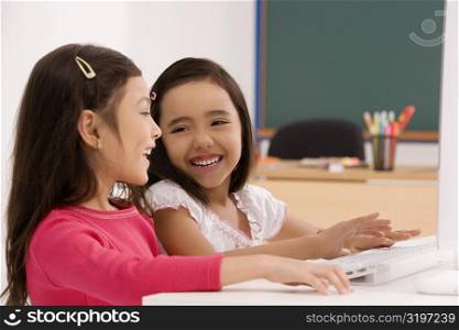 Two schoolgirls smiling in front of a computer