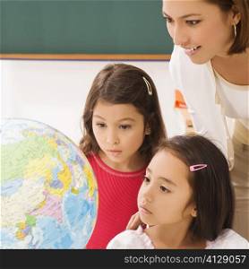 Two schoolgirls with a female teacher looking at a globe