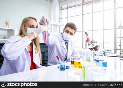 Two scientists are working holding looking at test tube with s&le in a chemistry lab scientist or young female and male researcher are doing investigations in Laboratory analysis background