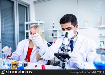 Two scientists are working holding looking at test tube with s&le in a chemistry lab scientist or young female and male researcher are doing investigations in Laboratory analysis background