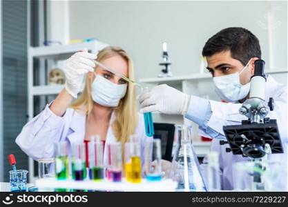 Two scientists are working holding looking at test tube with sample in a chemistry lab scientist or young female and male researcher are doing investigations in Laboratory analysis background