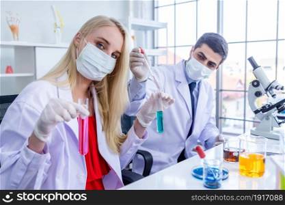 Two scientists wears hygiene protective mask are working holding looking at test tube with sample in a chemistry lab scientist are doing investigations in Laboratory analysis background