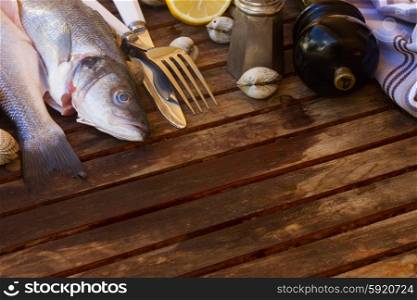 Two Seabass raw fish with seashells, copy space on wooden table planks