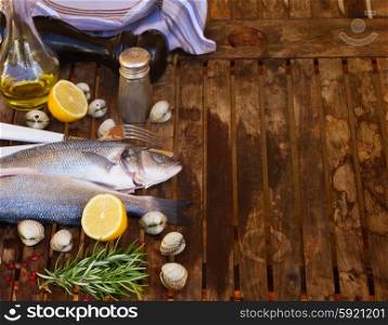 Two Seabass raw fish with shellfish and spices, empty copy space on wooden table