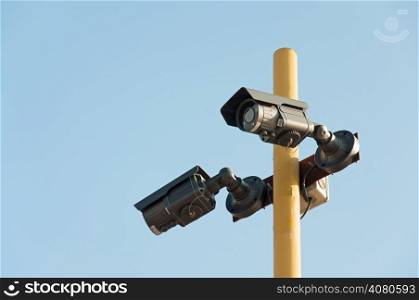 Two Security Camera of black color over background of a blue sky.