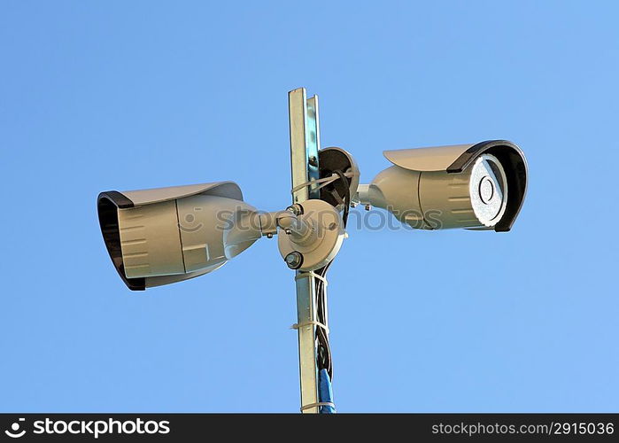 Two security cameras against blue sky