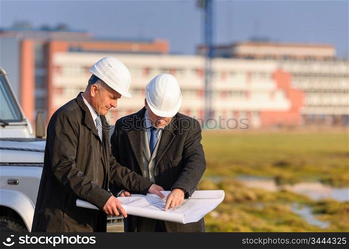 Two senior architect developers review plans at a construction site