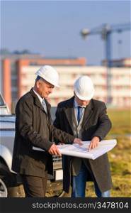 Two senior architect developers review plans at a construction site
