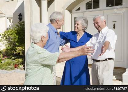 Two senior couples greeting each other with open arms