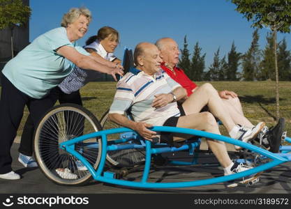 Two senior men sitting on a quadracycle and two senior women pushing it