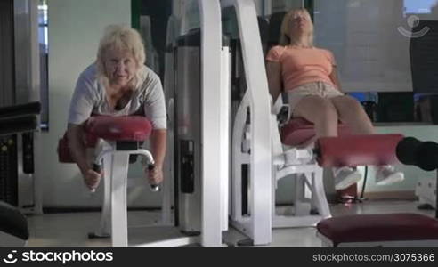 Two senior women having a workout in the gym. They using front and back leg curl machines. Going in for sport to keep fit and healthy
