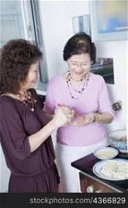 Two senior women preparing Chinese dumplings in a kitchen