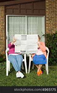 Two senior women sharing a newspaper