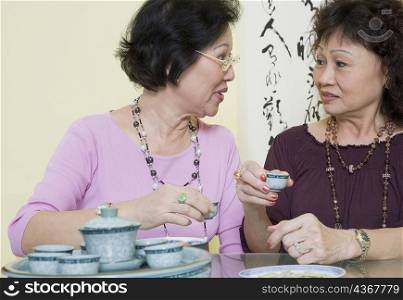 Two senior women sitting at a table and holding tea cups
