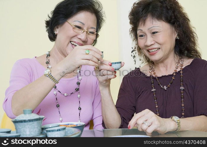 Two senior women sitting at a table and toasting with tea cups