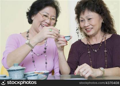 Two senior women sitting at a table and toasting with tea cups