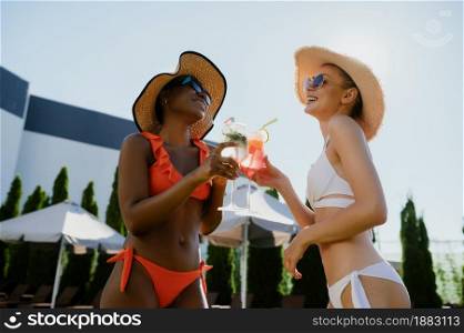 Two sexy girlfriends drink coctails at the pool. Happy people having fun on summer vacations, holiday party at the poolside outdoors. Women leisure. Two sexy girlfriends drink coctails at the pool