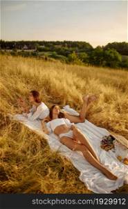 Two sexy women in lingerie relax on blanket in the field. Female persons with slim body in underwear leisures on meadow, relaxation on sunset, feeling of freedom. Sexy women in lingerie relax on blanket in field