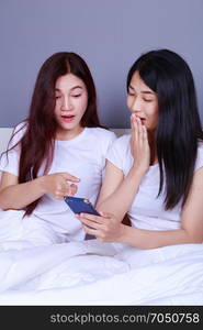 two shocked woman using a phone in her hand on bed in the bedroom