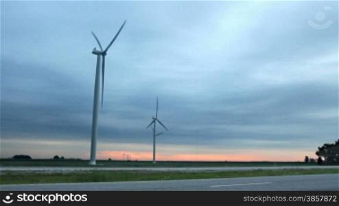 Two shots in one. A semi truck drives by wind turbines, and a closeup of the turbine against the sky.