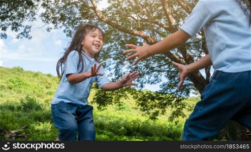 Two sibling little girls laughing and hugging each other on warm and sunny summer day in the garden. Young girls with her mother spending day in park.