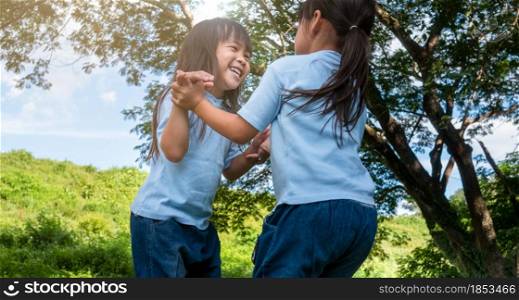 Two sibling little girls laughing and hugging each other on warm and sunny summer day in the garden. Young girls with her mother spending day in park.