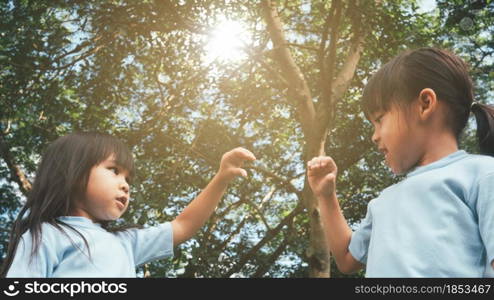 Two sibling little girls laughing and hugging each other on warm and sunny summer day in the garden. Young girls with her mother spending day in park.