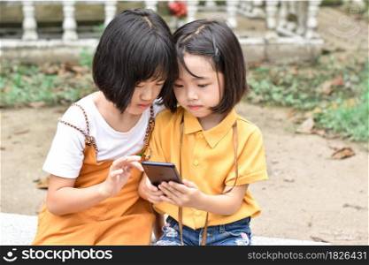 Two sister children holding smartphone and play games at park outdoor.