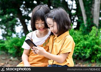 Two sister children holding smartphone and play games at park outdoor.