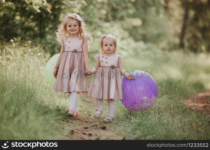 two sisters are playing balloons. Happy sister with balloons walking on the spring field. kids playing together. two sisters are playing balloons. kids playing together. Happy sister with balloons walking on the spring field