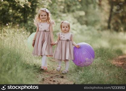 two sisters are playing balloons. Happy sister with balloons walking on the spring field. kids playing together. two sisters are playing balloons. kids playing together. Happy sister with balloons walking on the spring field